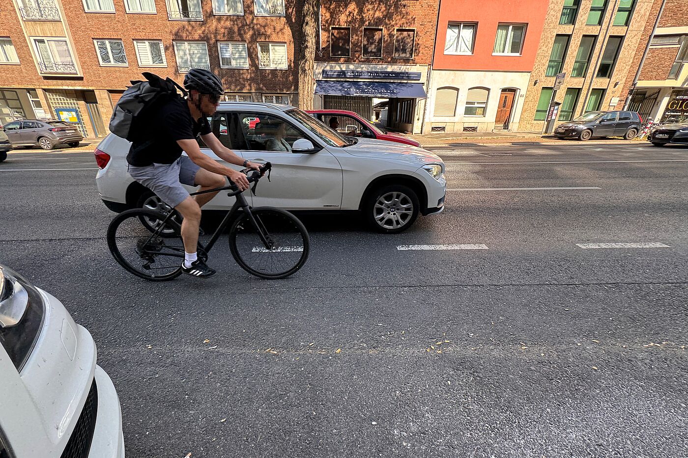 Enges Überholen auf der Wilhelmstraße Ein Radfahrer fährt auf der rechten Fahrspur der Wilhelmstraße neben einem weißen Auto. Die Straße ist mehrspurig, es gibt keinen baulich geschützten Radweg.