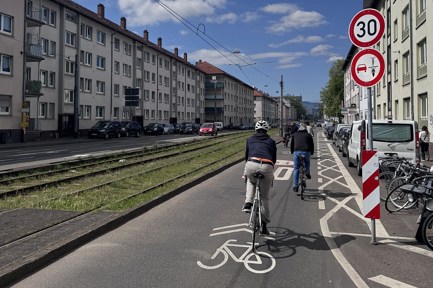Schloßstraße Frankfurt: Mögliche Übergangslösung Radfahrende fahren auf einer Fahrbahn mit Fahrradpiktogrammen. Ein Verkehrszeichen weist auf Tempo 30 und ein Überholverbot gegenüber einspurigen Fahrzeugen hin.