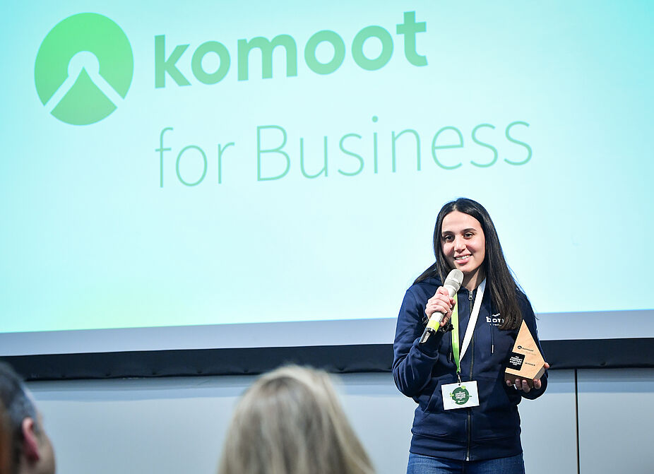 2025_komoot-Partner-Awards-2024-Vergabe-Rede_Gabriele-Giessenboeck Frau redet in Mikrofon mit komoot Partner Award 2024 in der Hand