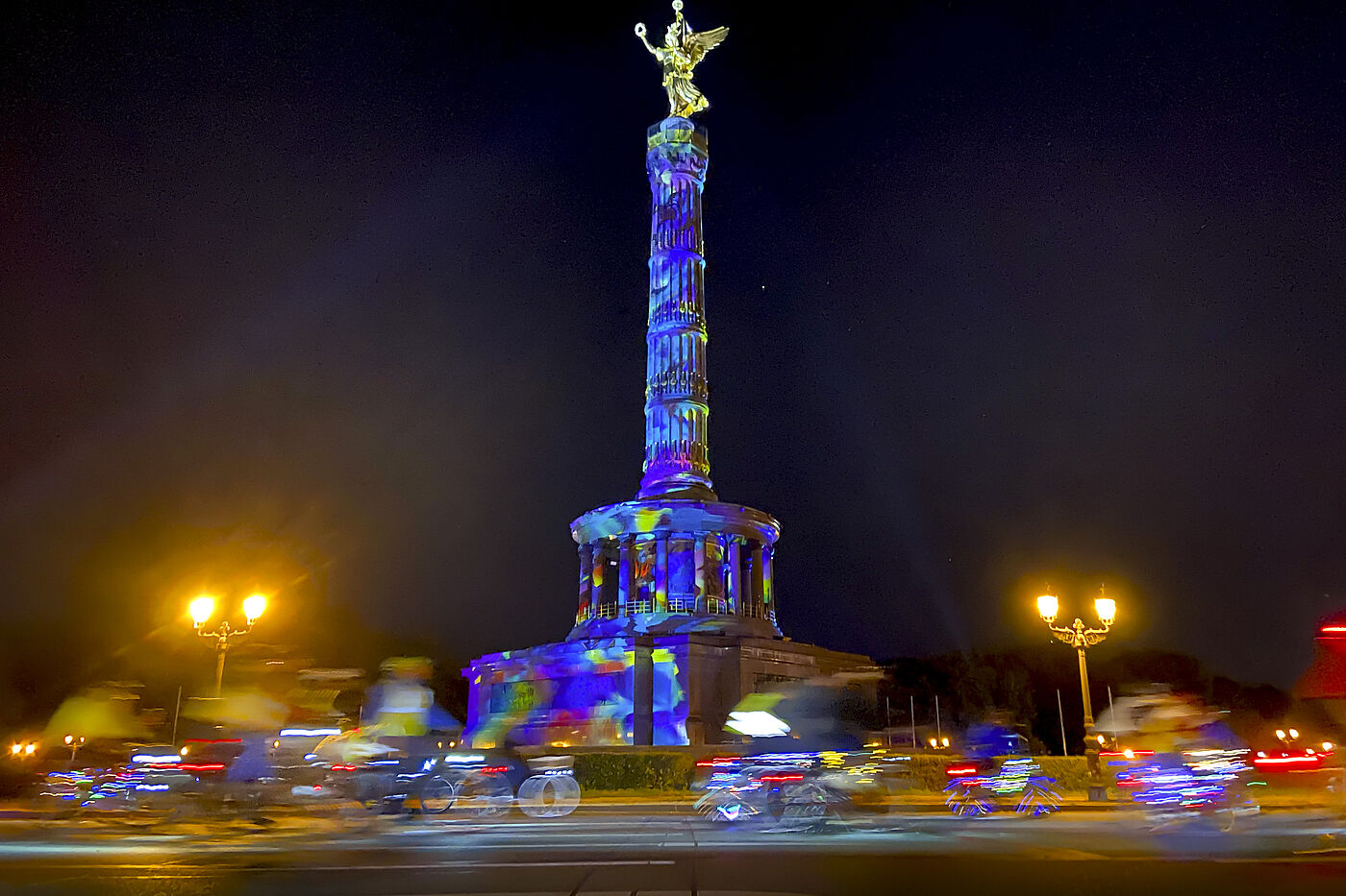 Lichterfahrt 2024 Menschen auf Fahrrädern fahren im Dunklen um die bunt angestrahlte Siegessäule