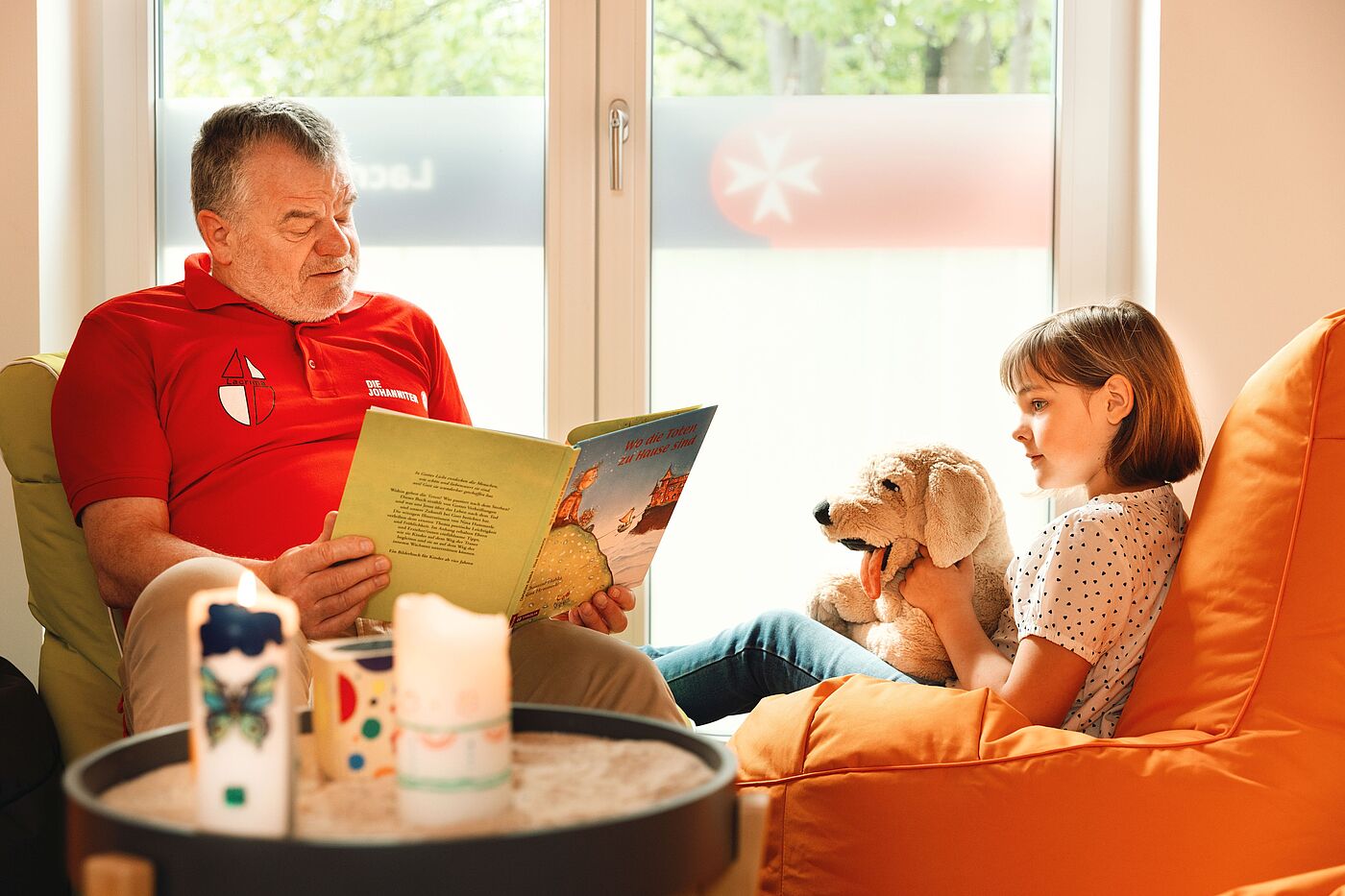 Johanniter Lacrima Trauerbewältigung Ein Mann liest einem Mädchen mit einem Stofftier ein Buch vor
