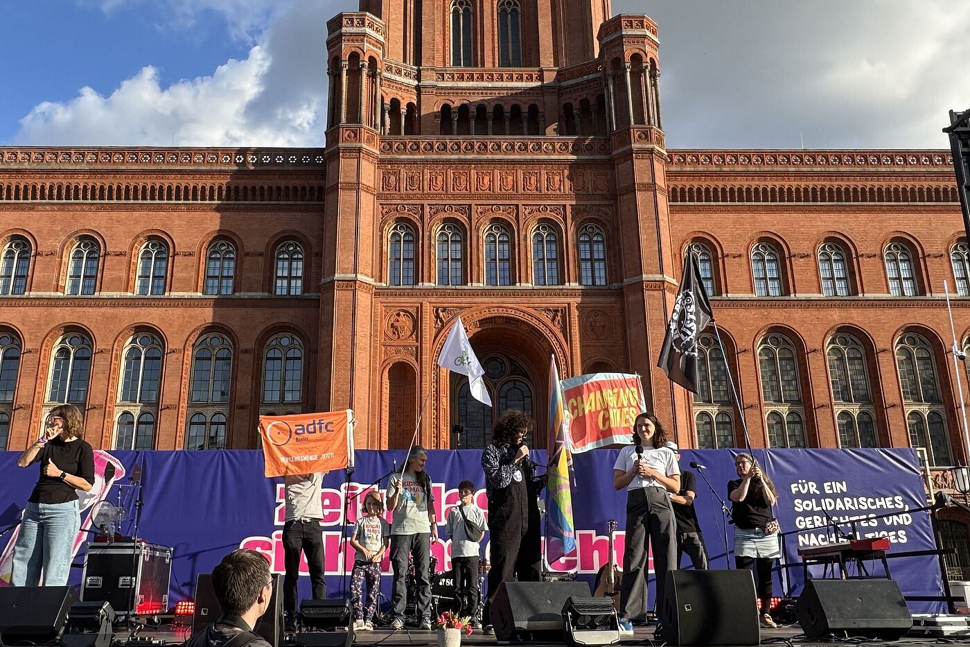 Abschlusskundgebung vor dem Brandenburger Tor Im Hintergrund ist das Rote Rathaus, davor eine Bühne, auf der zwei Personen sprechen und Fahnen von Changing Cities und ADFC Berlin zu sehen sind.