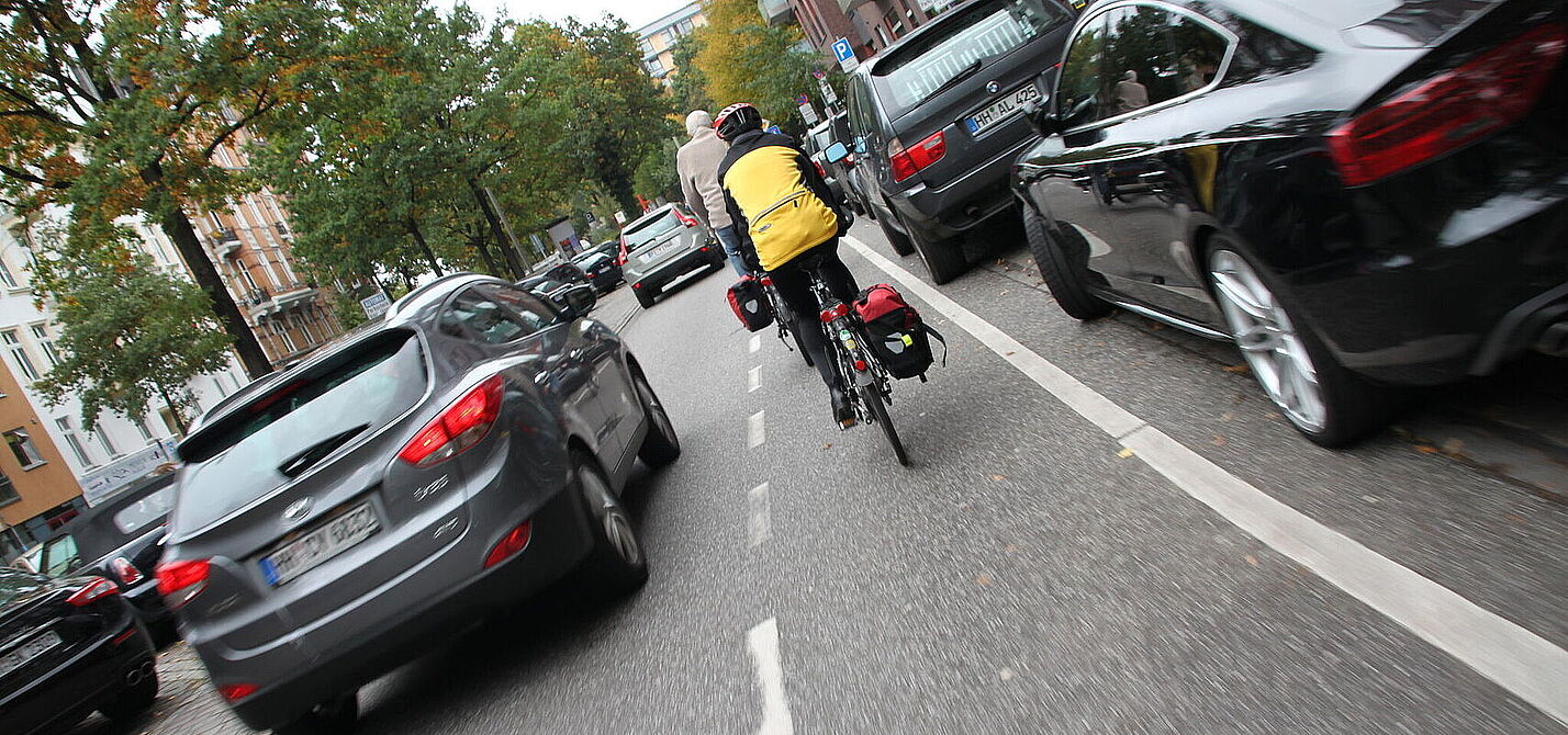 Radfahrende auf schmalem Schutzstreifen werden zu eng überholt Radfahrender fährt neben parkenden Autos und wir von fahrenden Kfz zu knapp überholt.