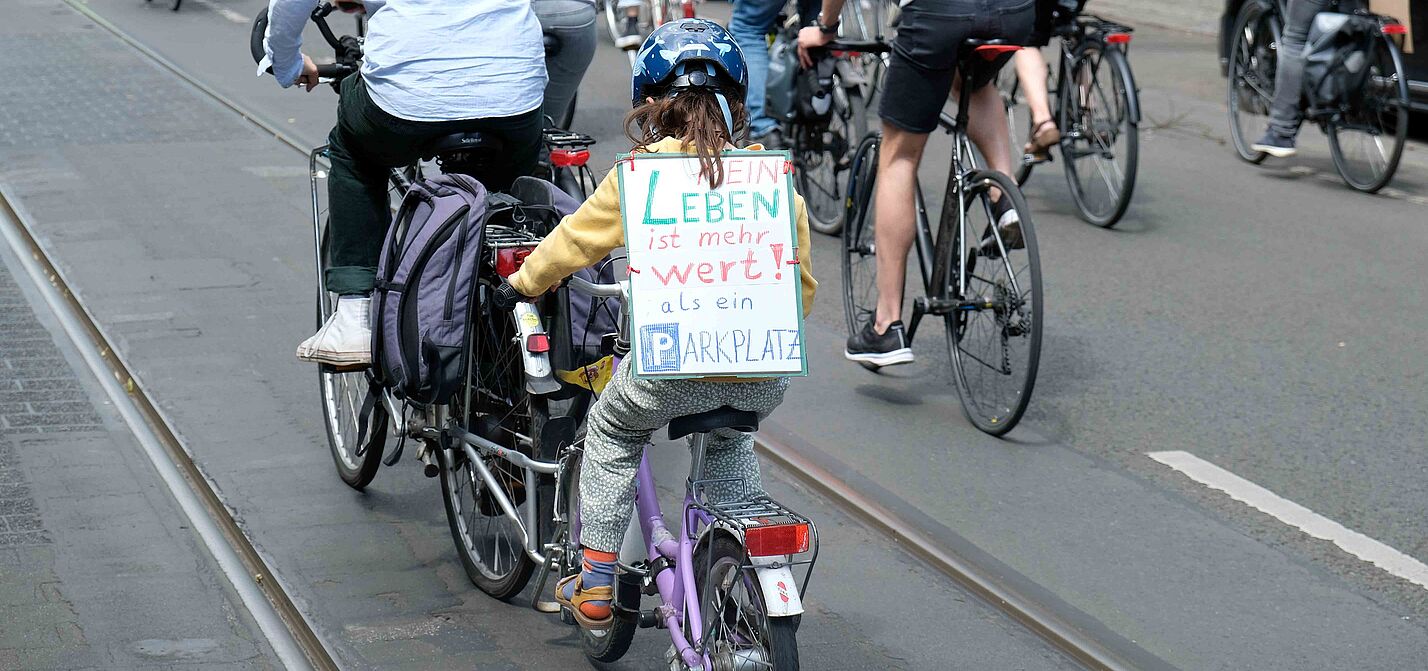 Mädchen auf Fahrrad mit einem Schild auf dem steht: Mein Leben ist mehr wert als ein Parkplatz