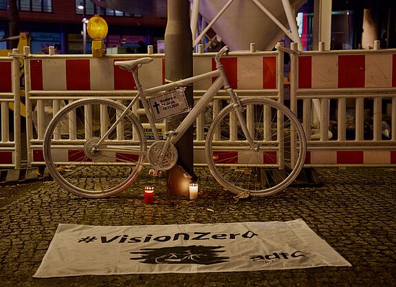 Geisterrad 24.11.2025 Mitte Ein weißes Geisterrad an einem Laternenphal davor eine weiße Vision Zero Fahne