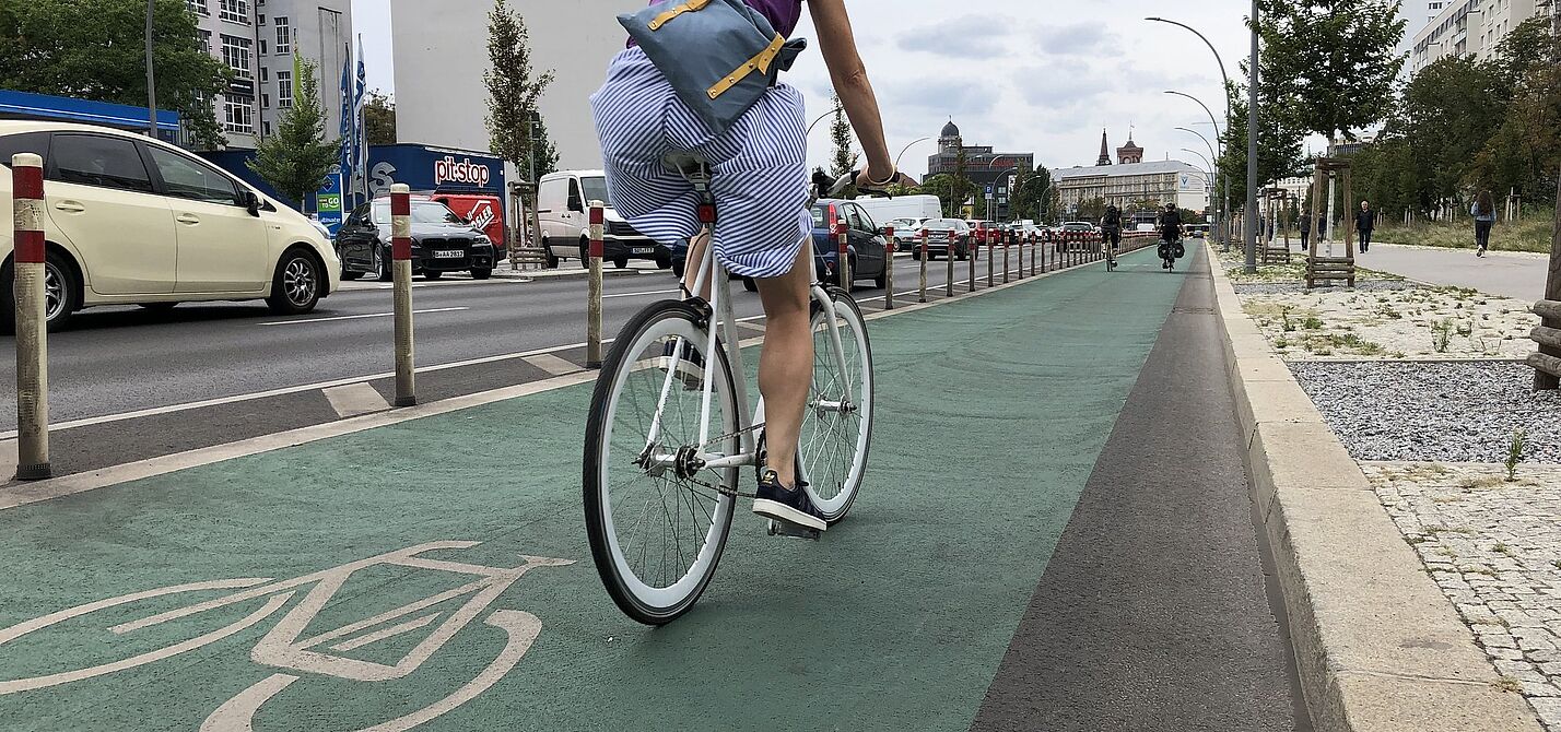 Radfahrstreifen Eine Frau fährt auf einem grün markierten Radfahrstreifen mit Pollern vom Autoverkehr getrennt.