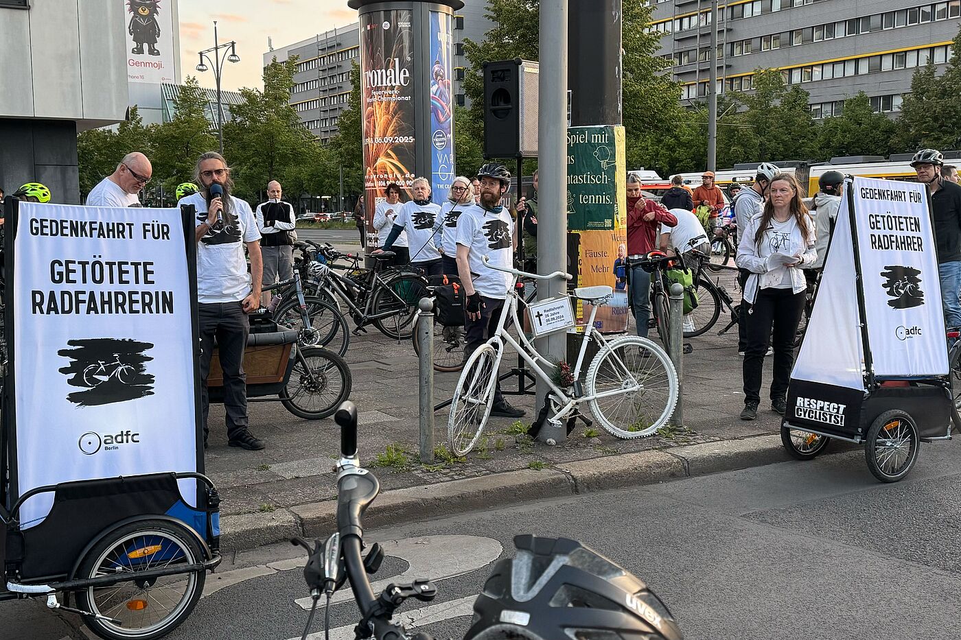 Ride of Silence 2025 Menschen halten am Straßenrand eine Rede zwischen zwei Schildern "Gedenkfahrt für getötete Radfahrerin"