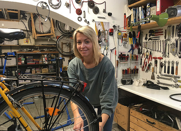 Fahrradwerkstatt Das Bild zeigt eine junge Frau, die in einer Fahrradwerkstatt an einem Rad arbeitet