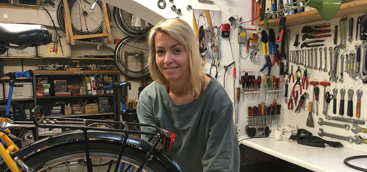 Fahrradwerkstatt Das Bild zeigt eine junge Frau, die in einer Fahrradwerkstatt an einem Rad arbeitet