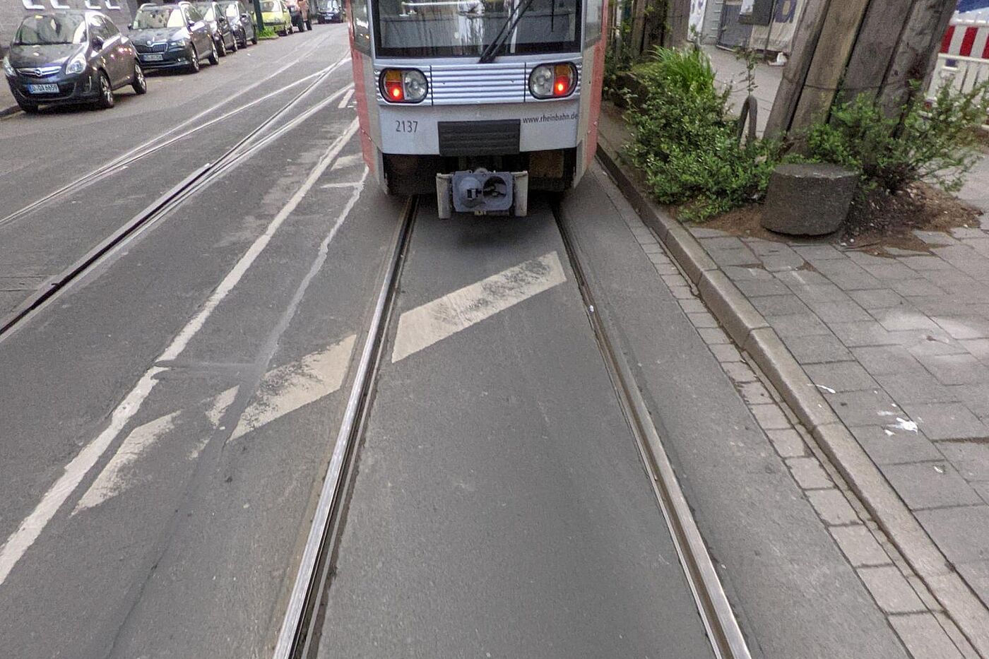 Das Bild zeigt einen Radfahrer, welcher zwischen den Straßenbahnschienen fährt. Davor ist eine Straßebahn, welche an einer Haltestelle hält