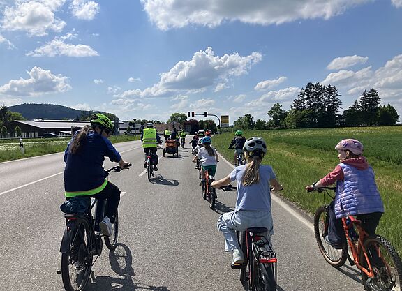 Die Fahrraddemo unterwegs auf der Landesstraße, die Kamera fährt hinter mehreren Kindern und einem Erwachsenen