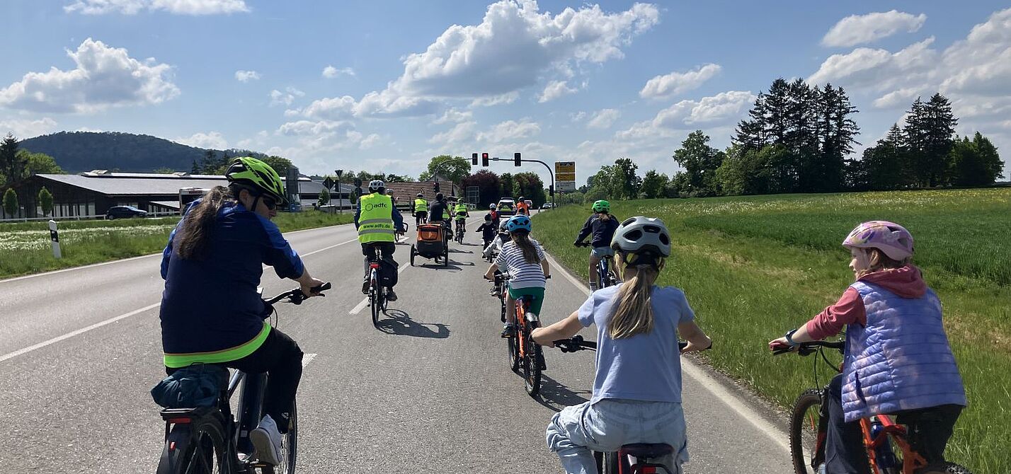 Die Fahrraddemo unterwegs auf der Landesstraße, die Kamera fährt hinter mehreren Kindern und einem Erwachsenen