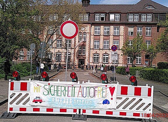 Schulstraße RH 2023 Absperrung Das Bild zeigt die Sperre an der Schulstraße mit einem von Kindern gemalten Transparent mit der Aufschrift 'Mit Sicherheit Autofrei'