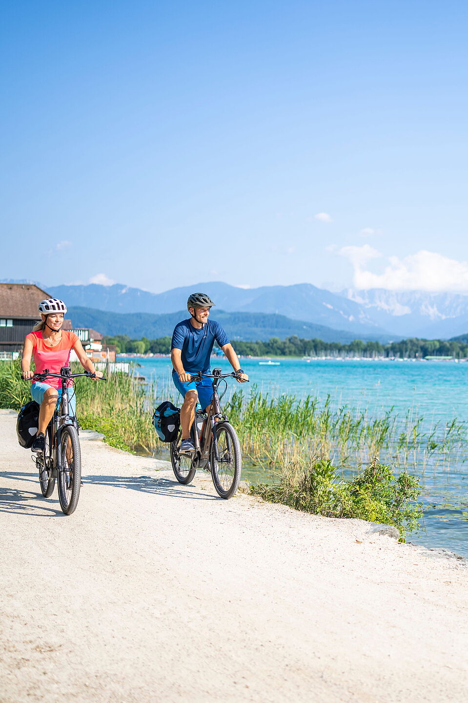 Radfahren am Wörthersee Zwei Radfahrende auf Uferweg am türkisfarbenen See mit Bergpanorama im Hintergrund.