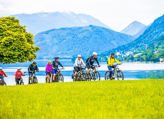 Radtour in der Gruppe am See Gruppe von Radfahrenden auf Wiese am See mit Bergpanorama im Hintergrund.