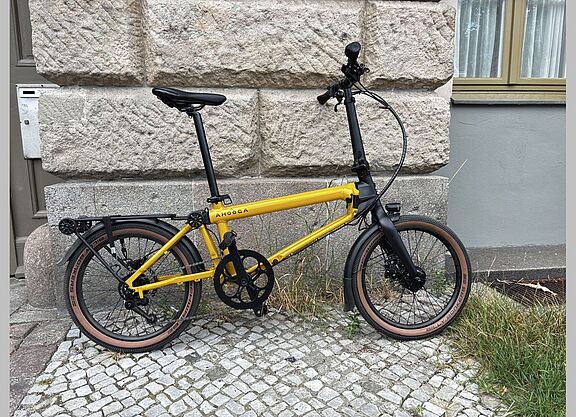 Ein gelb-schwarzes Faltrad steht vor einer Hauswand. 
