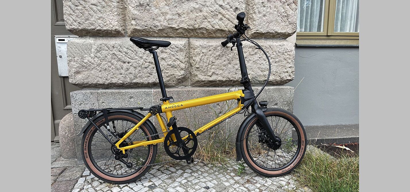 Ahooga E-Max Aufmacher Ein gelb-schwarzes Faltrad steht vor einer Hauswand.