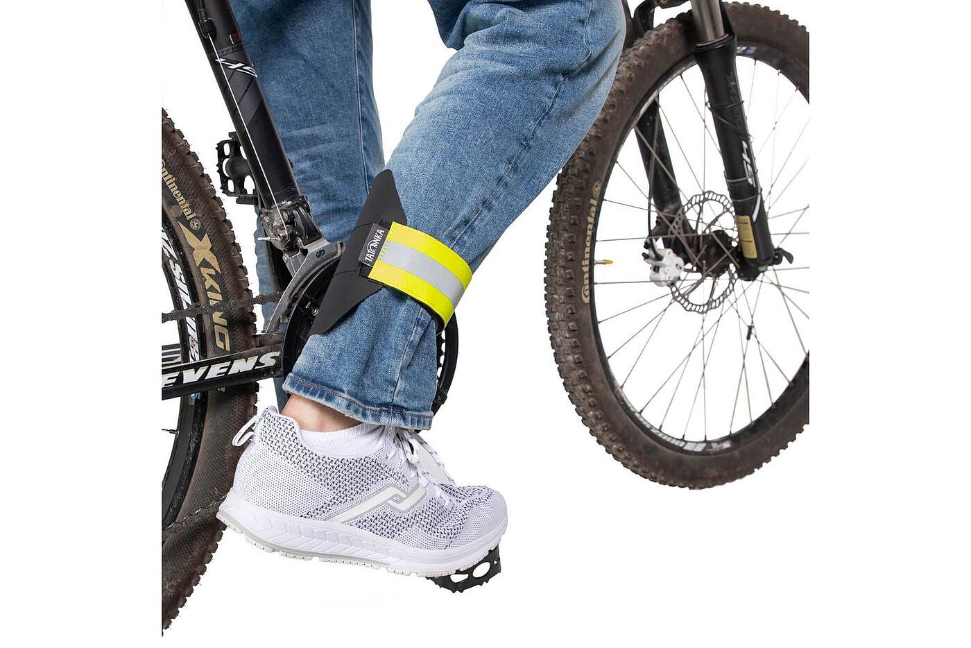 Tatonka Hosenschutz Ein Hosenbein wird beim Radfahren mit einem gelb reflektierenden Klettband am Bein fixiert; zu sehen sind das Fahrrad und der Fuß auf dem Pedal.