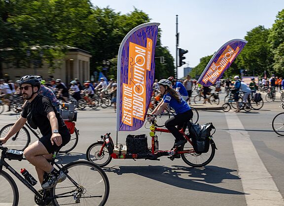 Viele Menschen auf Fahrrädern. An einem Rad befindet sich eine große Fahne mit dem Wort "Radvolution" darauf.