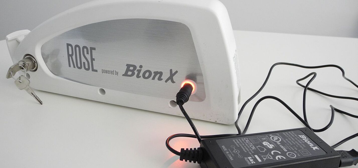 Alter Elektrorad-Akku Ein Elektrorad-Akku steht auf einem Tisch und ist am Netzteil angeschlossen.