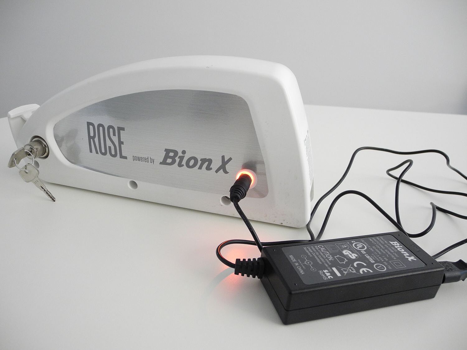 Ein Elektrorad-Akku steht auf einem Tisch und ist am Netzteil angeschlossen. 