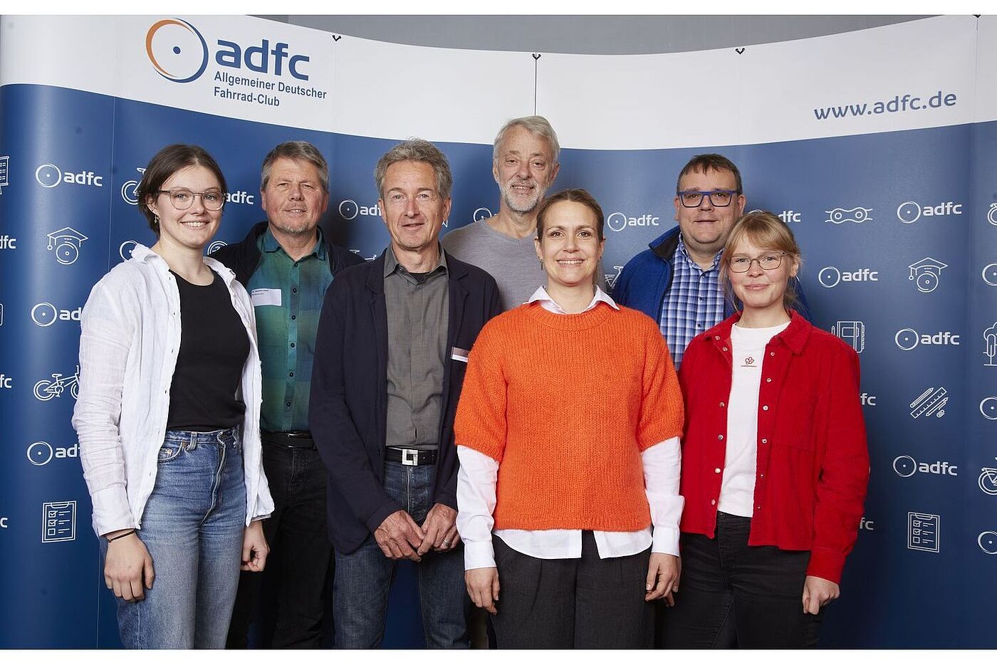 Vorstand Der neue ADFC-Bundesvorstand, von links nach rechts: Lena Adam, Dr. Joachim Lohse, Christian Tänzler, Frank Masurat, Sarah Holczer, Christoph Schmidt und Vera Konrad. Sie stehen vor einer blau-weißen ADFC-Fotowand.