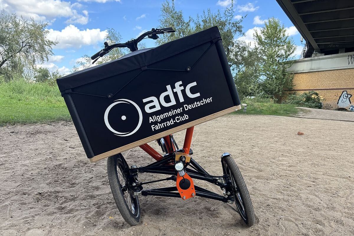Chike schräg Ein dreirädriges Lastenrad mit schräg geneigter Transportbox steht auf einem sandigen Weg.