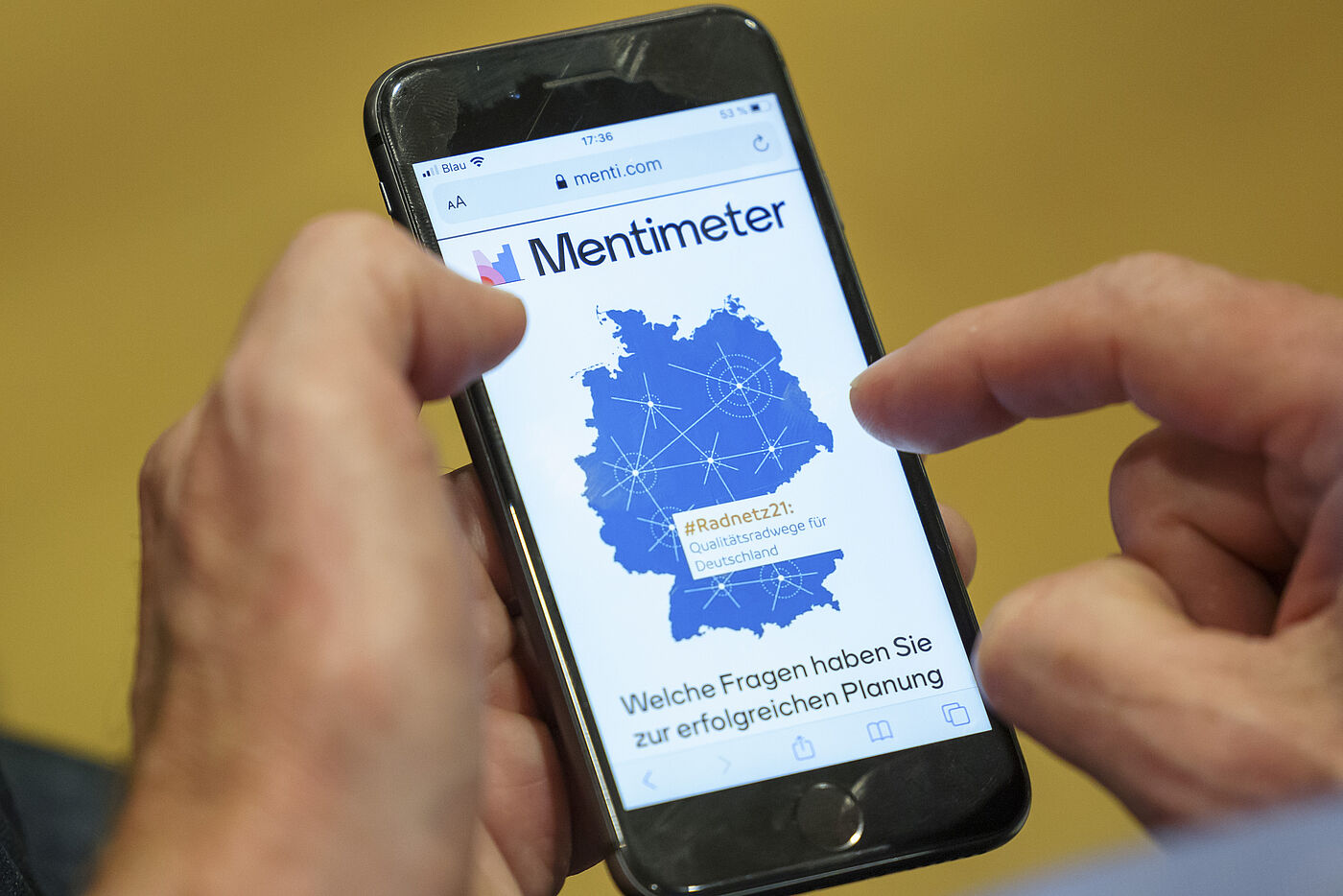 Mann hält ein Handy. Auf dem Handy ist die App Mentimeter zu sehen.