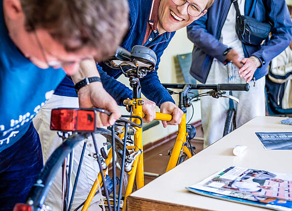 Menschen reparieren gemeinsam ein gelbes Fahrrad und lachen.