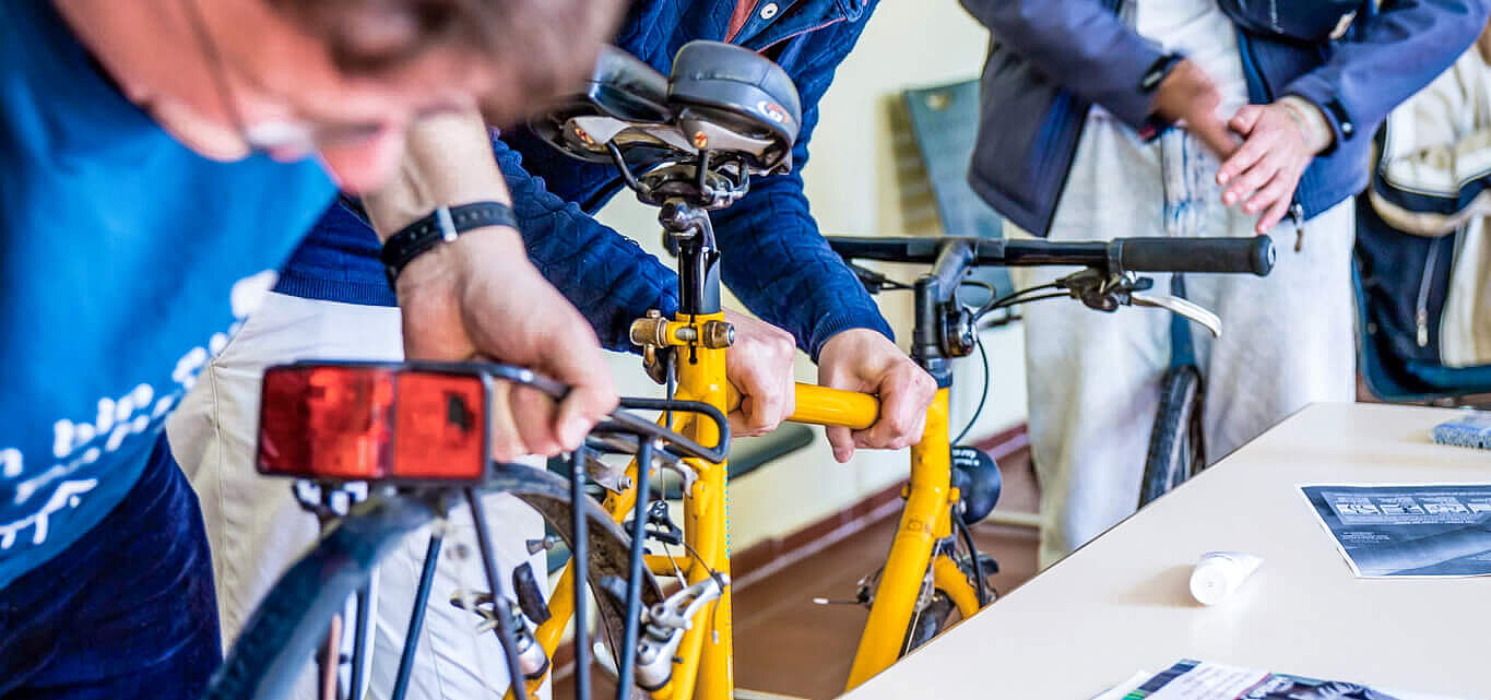 Junger ADFC Menschen reparieren gemeinsam ein gelbes Fahrrad und lachen.