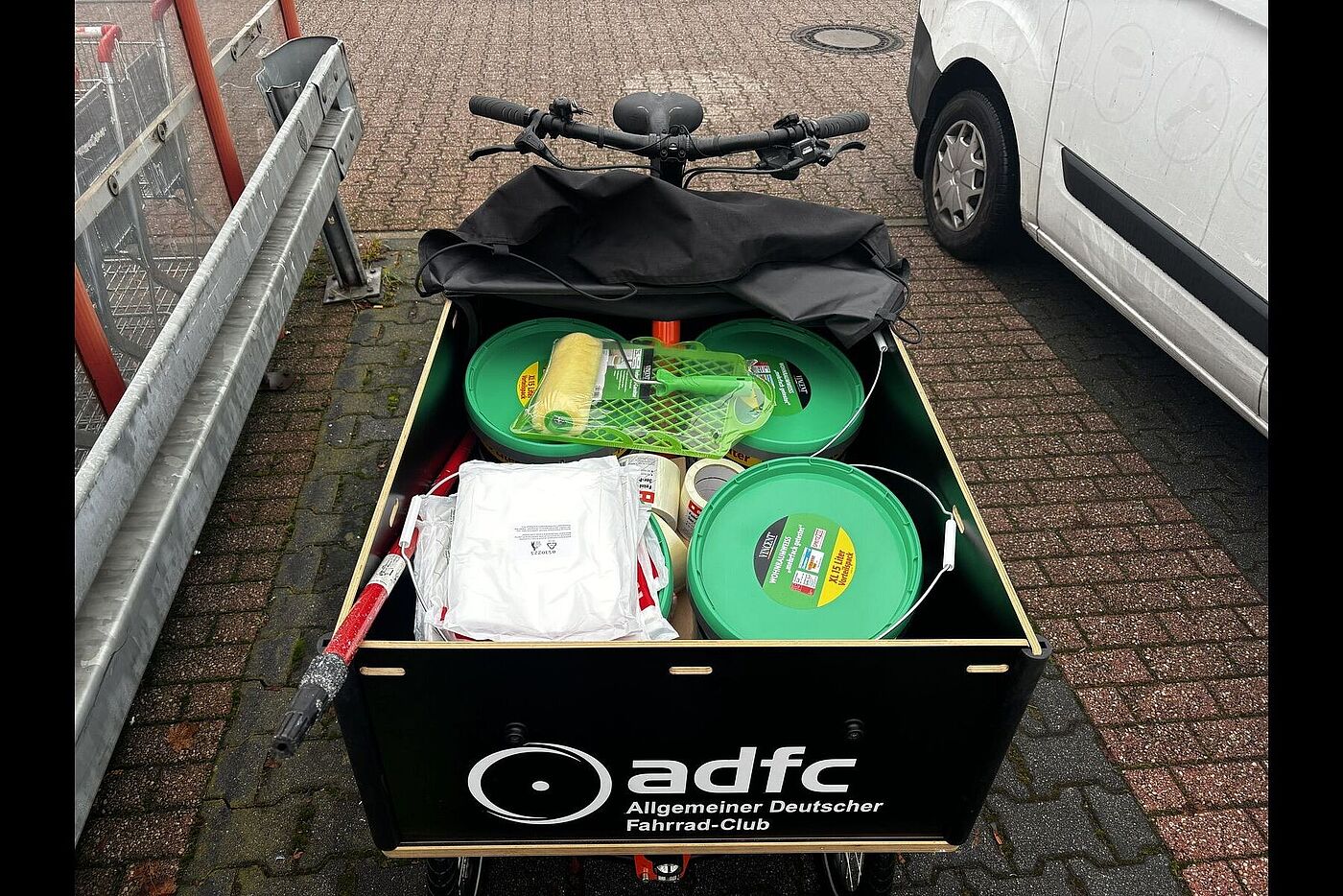Chike beladen Große Transportbox eines ADFC-Lastenrads, gefüllt mit Farbeimern, Rollen und weiterem Malerbedarf.