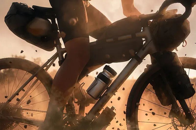 Eine Person fährt auf staubigem Untergrund im warmen Abendlicht, im Flaschenhalter steckt der Mokka to go-Kaffeebrüher. 