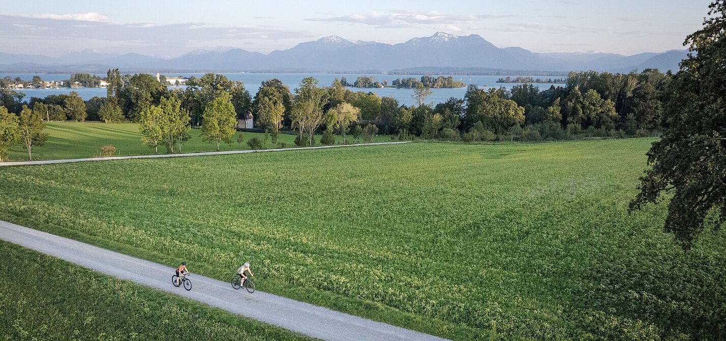 Zwei Personen fahren auf einem Radweg durch eine grüne Wiesenlandschaft.