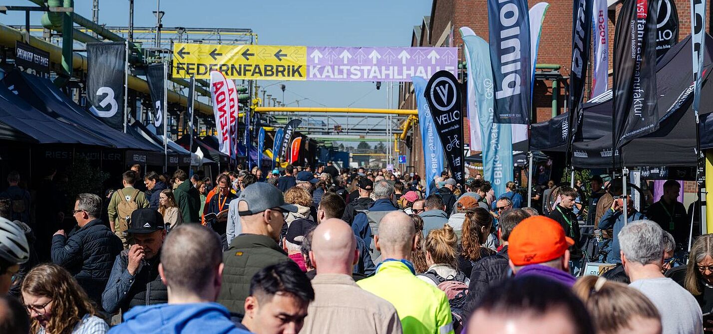 Eine Menschenmenge zwischen Ständen einer Fahrradmesse. 
