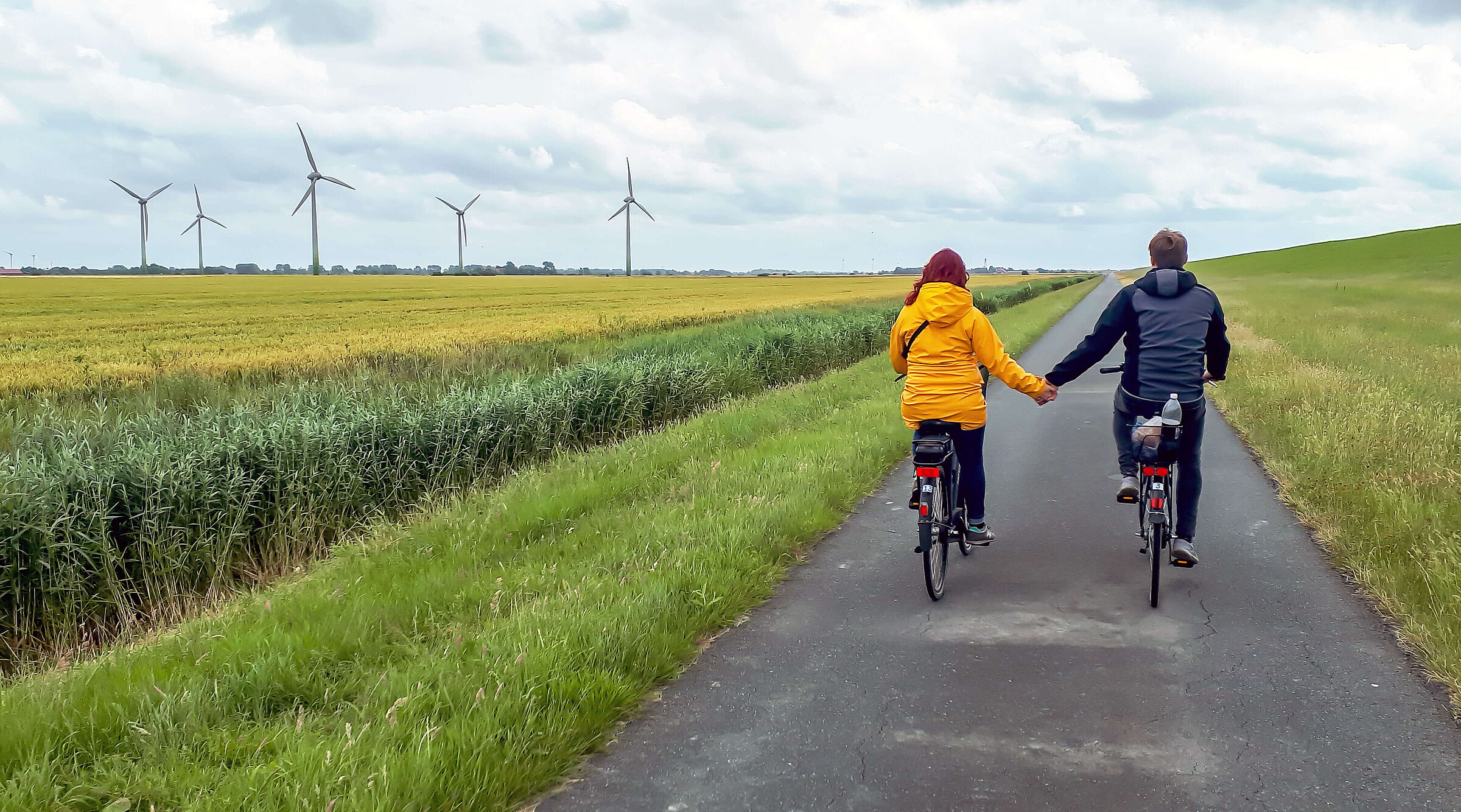 Zwei Radfahrende fahren auf einem asphaltierten Deichweg