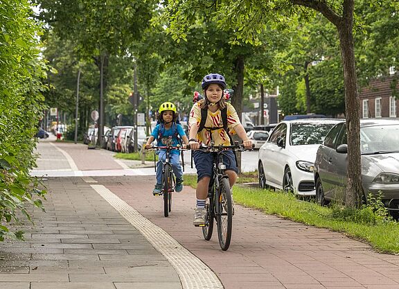 Ein Mädchen fährt vor einem Jungen auf dem Fahrrad auf einem Radweg.