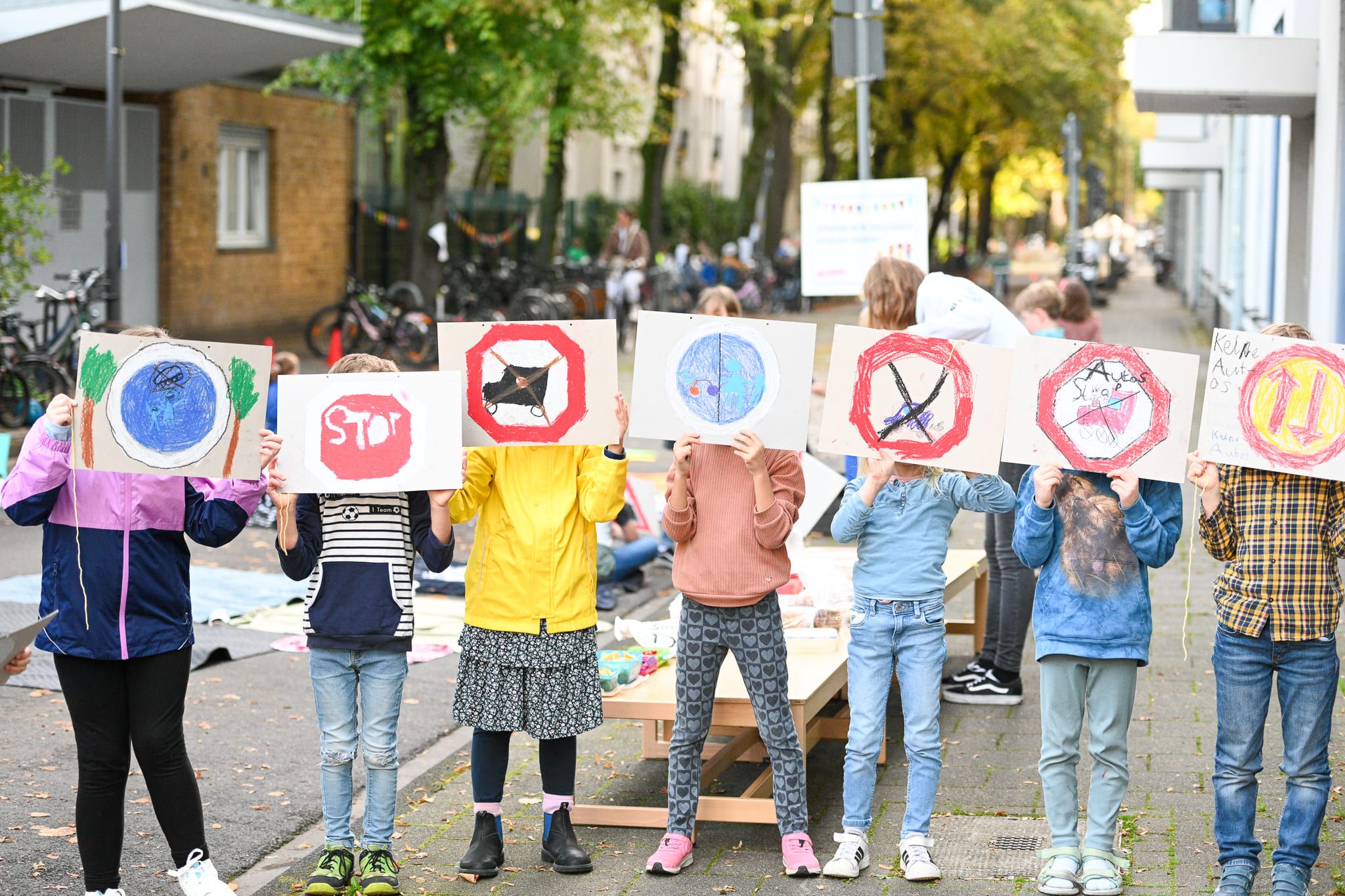 Kinder blockieren eine Straße, halten Plakate hoch und setzen sich damit für die Einrichtung von Schulstraßen ein.
