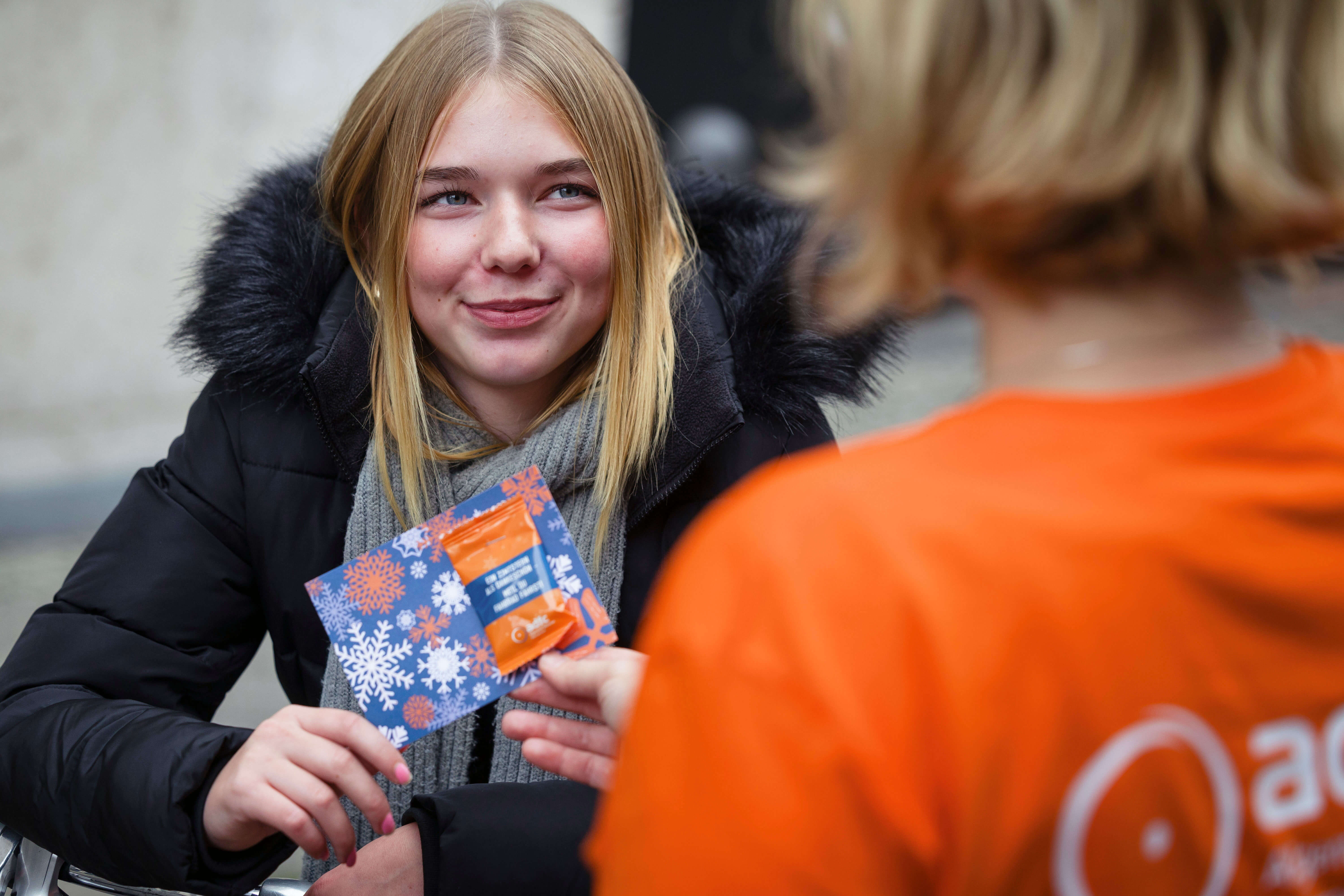 Eine lächelnde junge Frau in Winterjacke erhält von einer ADFC-Person eine blaue Karte mit Schneeflocken-Motiv und einen Zimtstern.