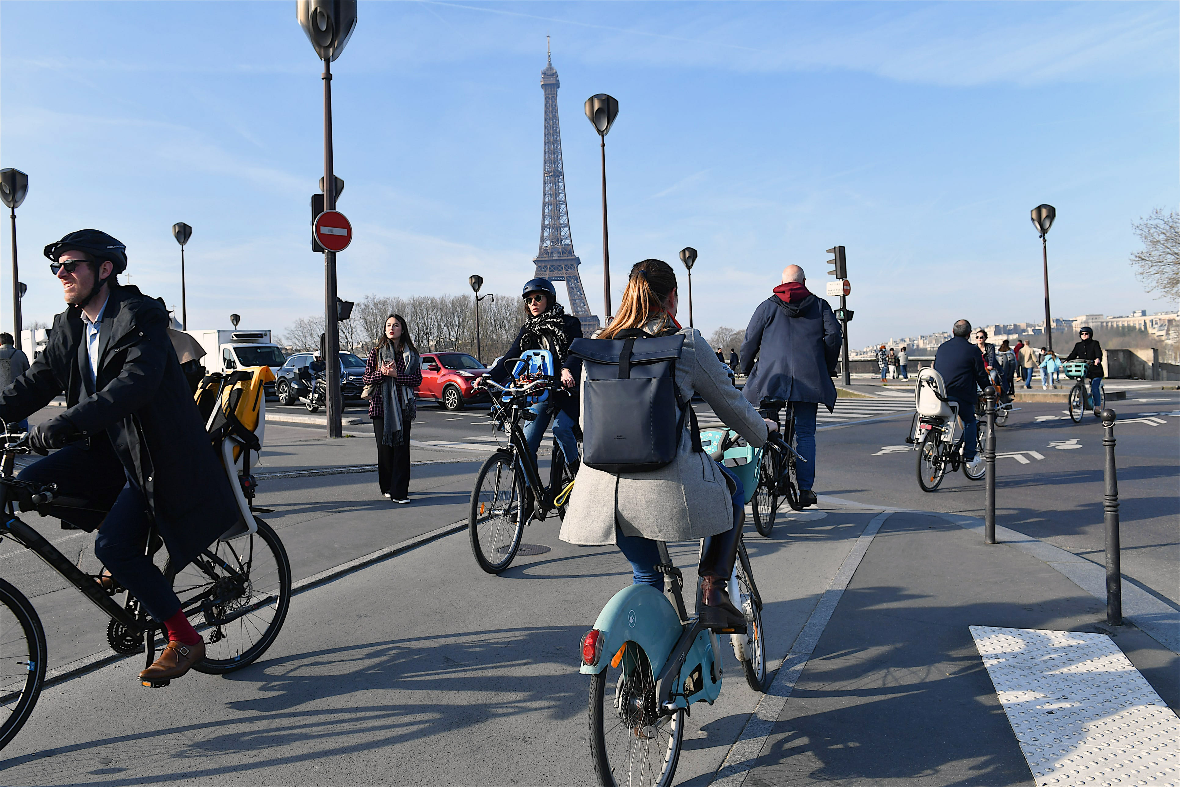 Menschen auf Fahrrädern überqueren eine Straße in Paris. Im Hintergrund ist der Eiffelturm zu sehen.