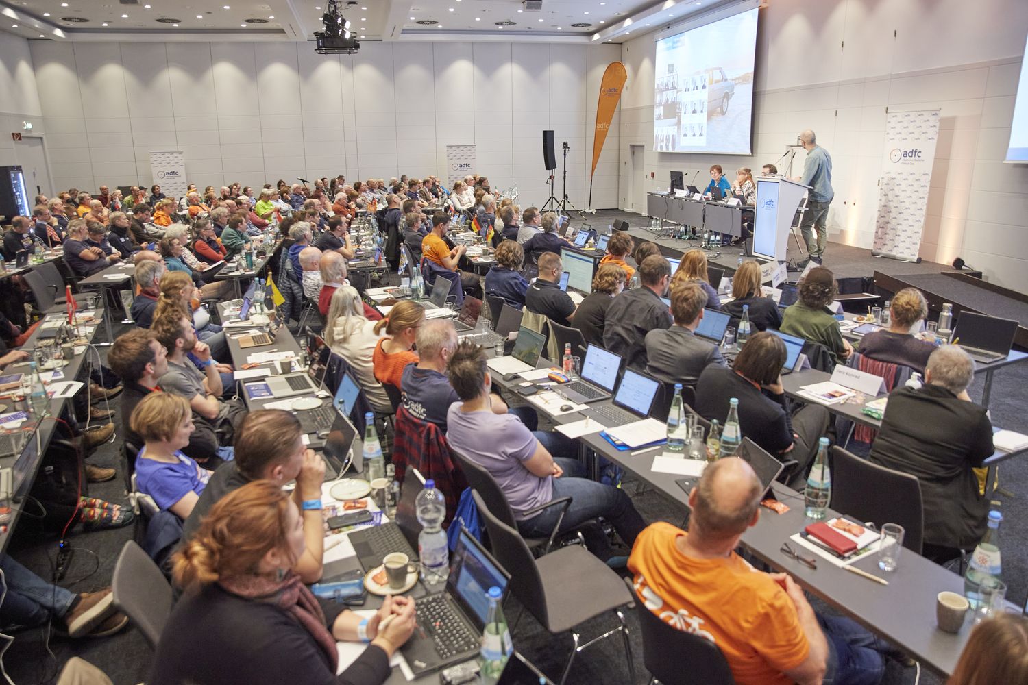 Ein grpßer Saal mit 140 Menschen an Tischreihen, die zur Bühne blicken, wo Boris von Heesen einen Vortrag hält. 