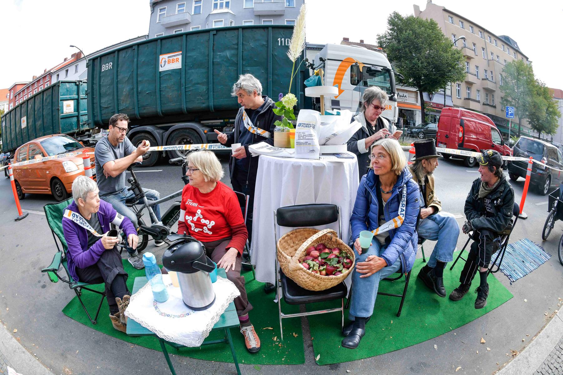 Auf dem Parking Day 2019 in Berlin-Tempelhof haben Menschen einen Tisch mit Kaffee und Obst aufgestellt und unterhalten sich in entspannter Atmosphäre.