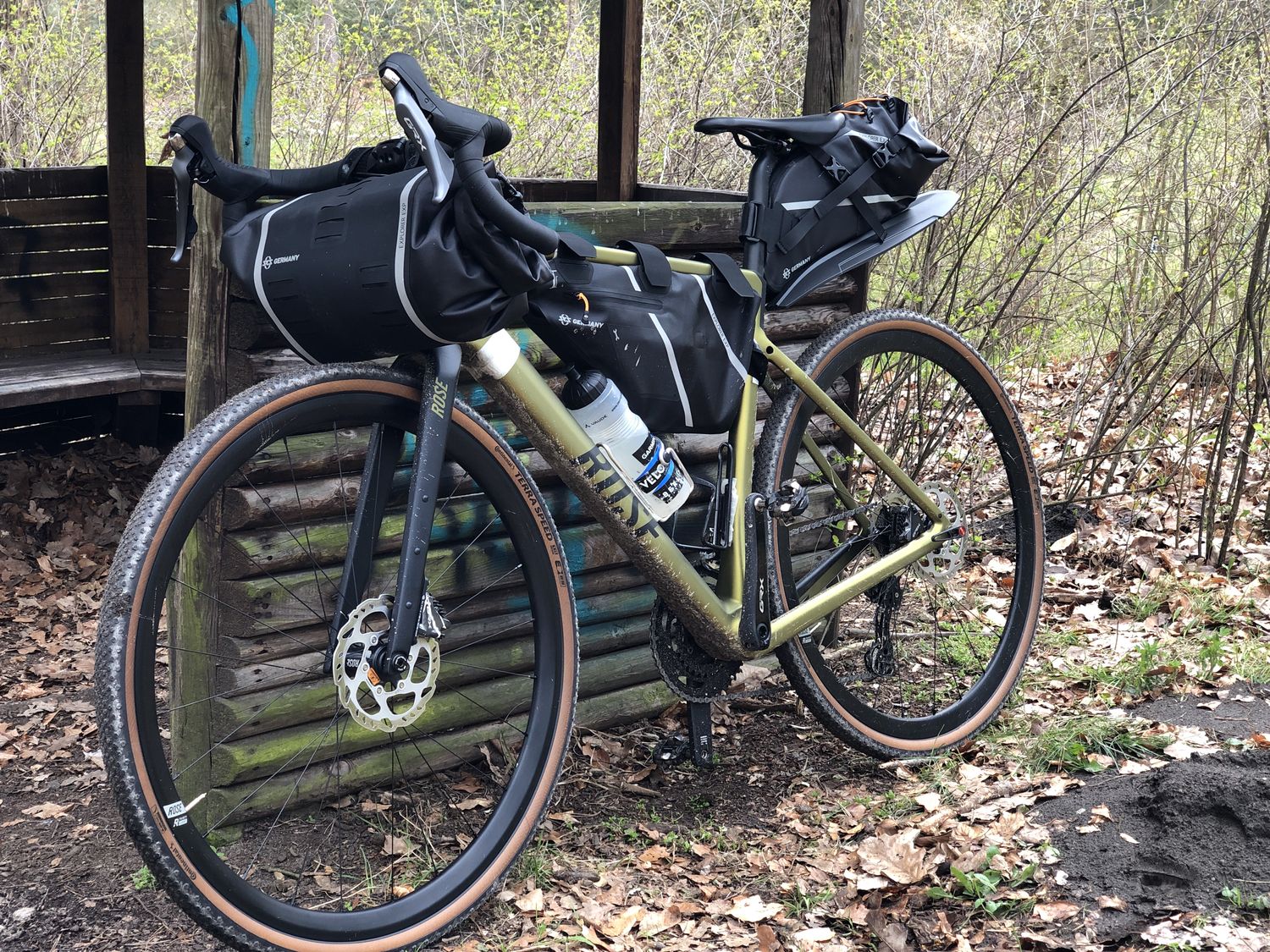 Ein Gravelbike mit Packtaschen lehnt an einer Schutzhütte im Wald. 