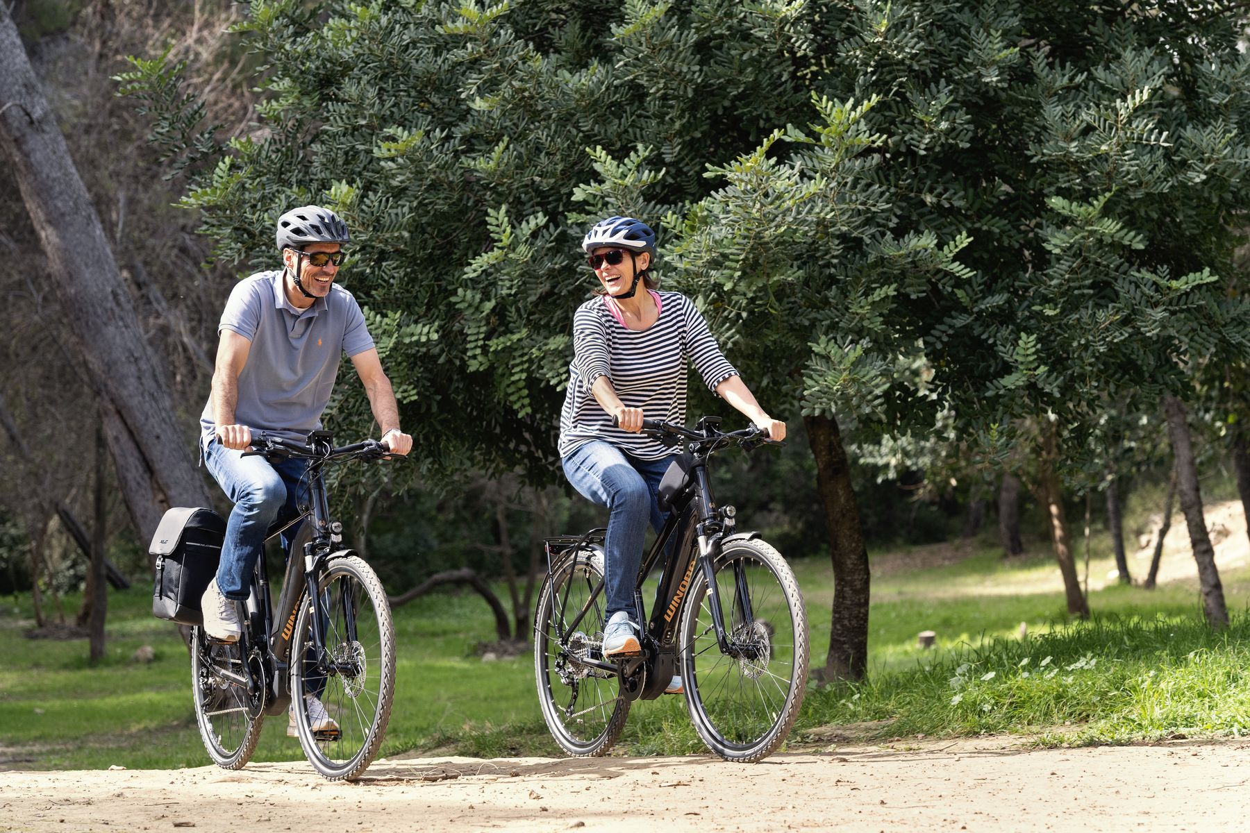 Eine Frau und ein Mann fahren auf Elektrofahrrädern durch den Wald. 