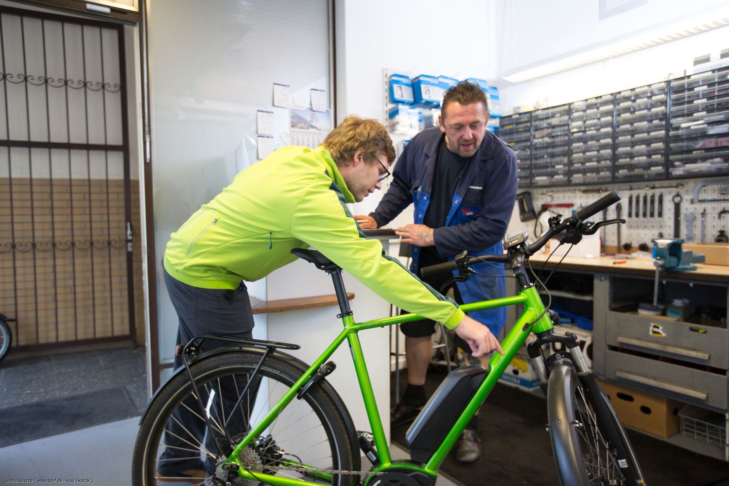 Ein Kunde zeigt dem Mechaniker in einer Werkstatt einen Defekt am Rad. 
