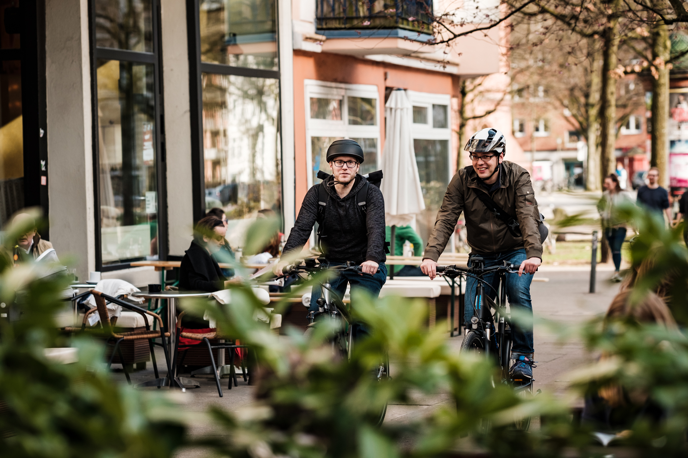 Zwei Männer mit Helm fahren auf einem Radweg im urbanen Raum