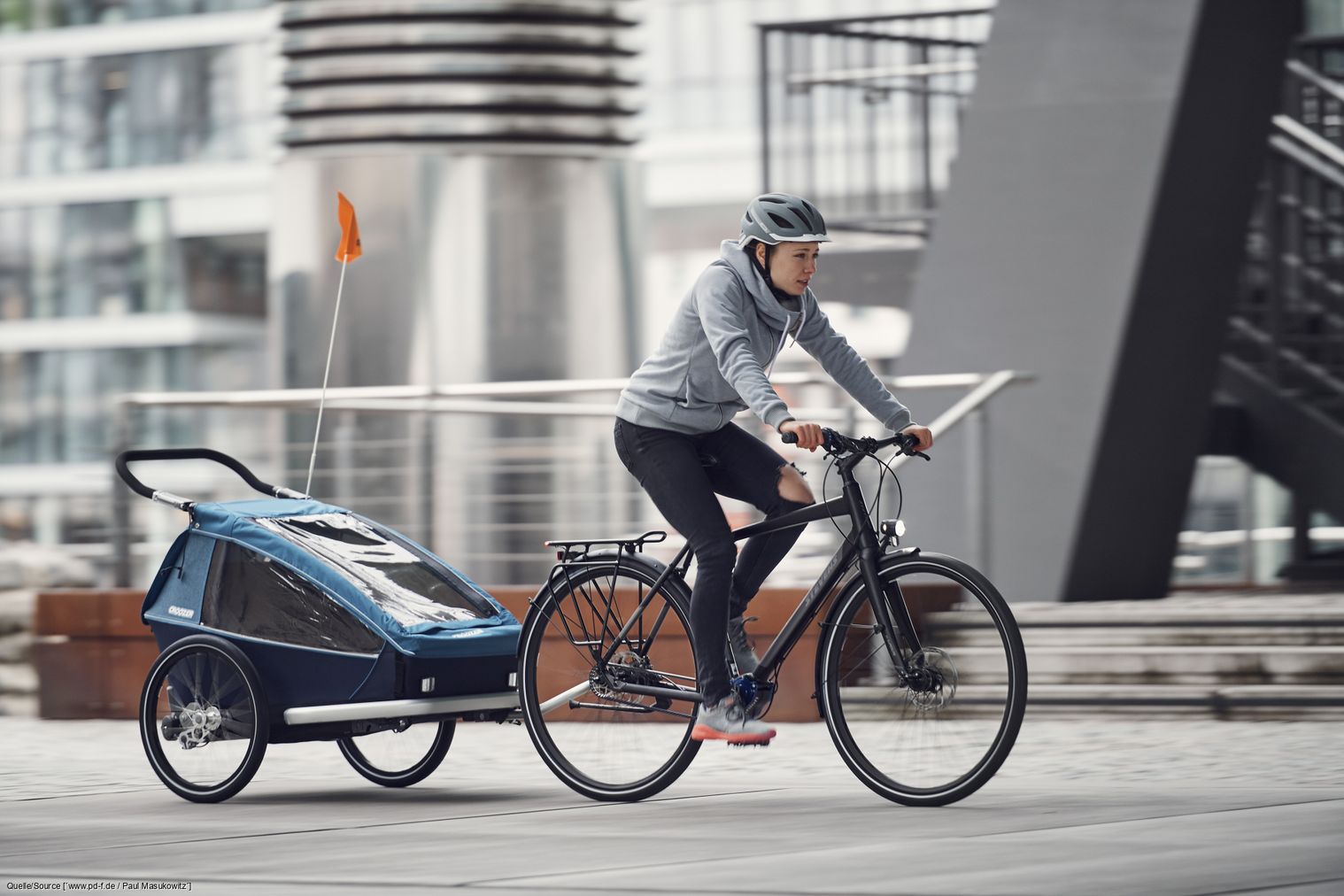 Eine Frau fährt auf einem Fahrrad mit einem Kinderanhänger.