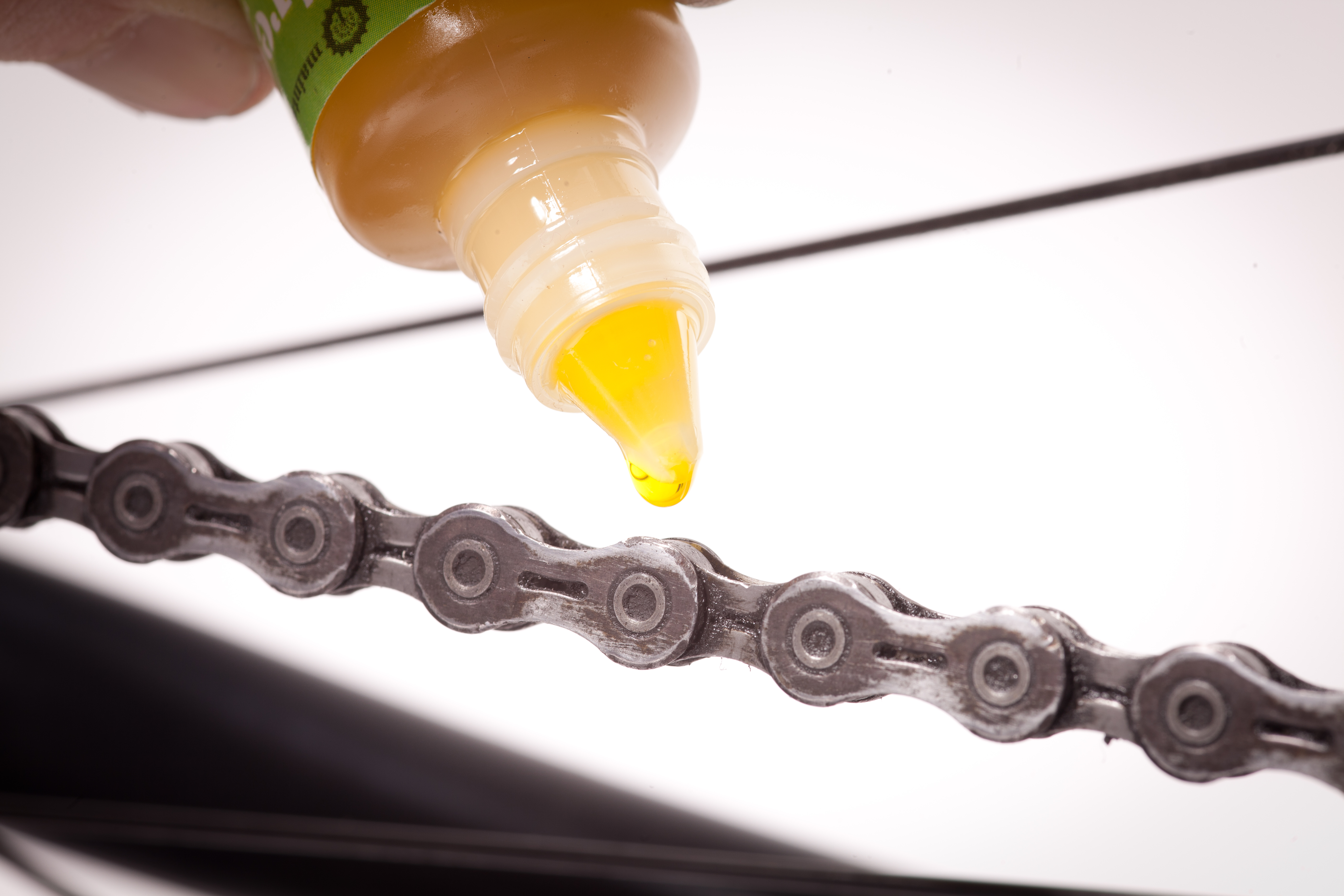 Großaufnahme eines Ölfläschchens, das an eine Fahrradkette gehalten wird. 