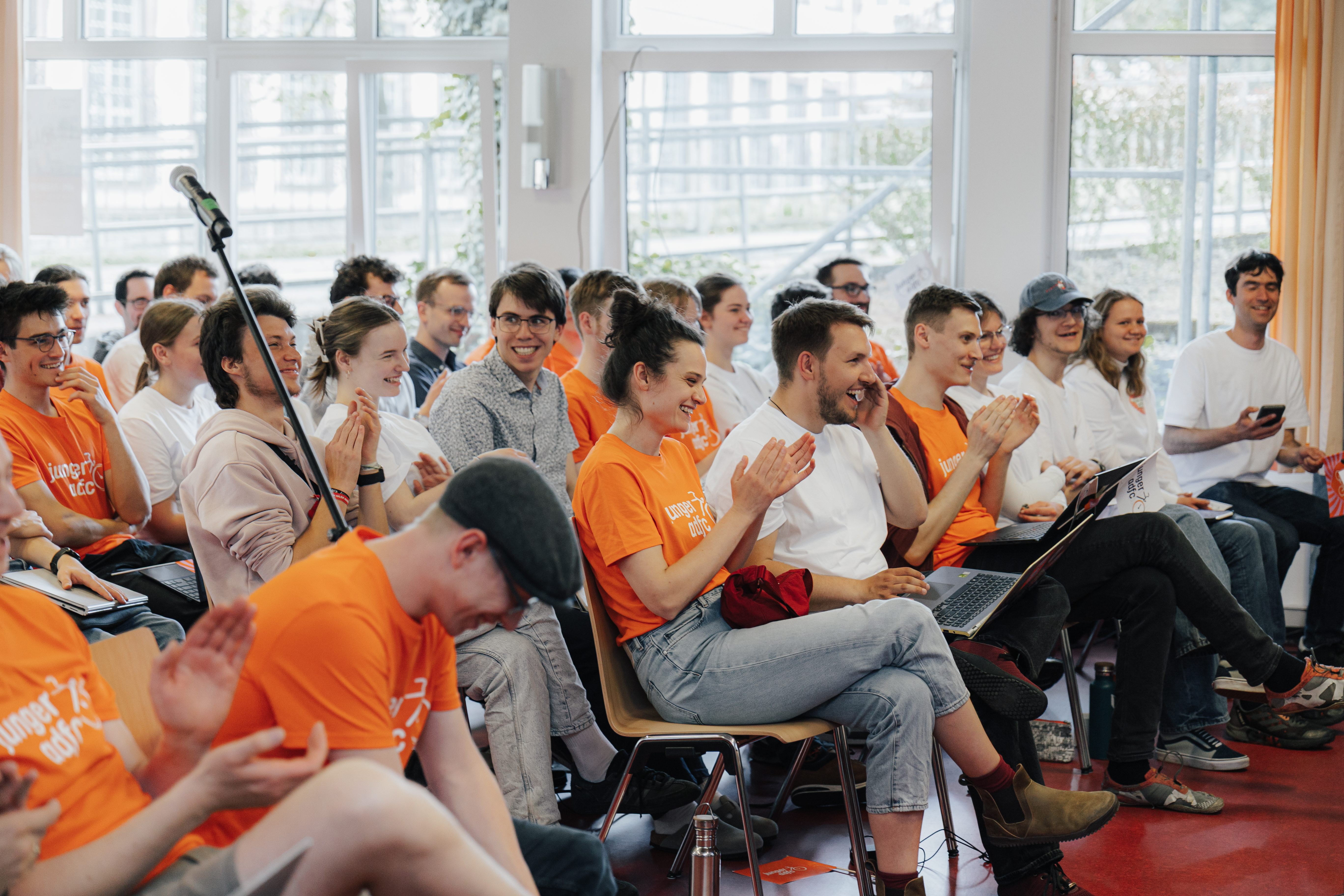 Junge Erwachsene sitzen in Stuhlreihen in einem Saal und heben grüne Stimmkarten in die Höhe.