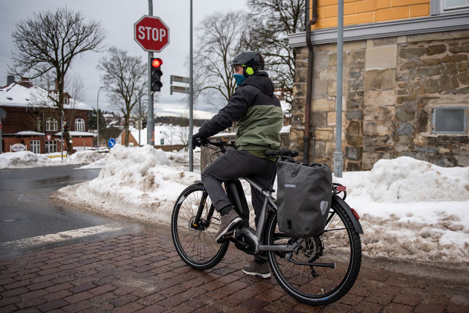 Ein Mann steht mit Fahrrad an einer Ampel in winterlicher Stadtlandschaft. 